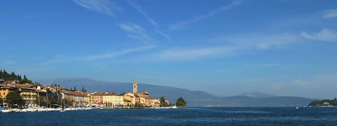 Lastminute Reisen beliebte Urlaubsziele am Gardasee -  Mit einer Fläche von 370 km² ist der Gardasee der größte See Italiens. Es liegt am Fuße der Alpen und erstreckt sich über drei Staaten: Lombardei, Venetien und Trentino. Die maximale Tiefe des Sees beträgt 346 m, er hat eine längliche Form und sein nördliches Ende ist sehr schmal. Dort ist der See von den Bergen der Gruppo di Baldo umgeben. Du trittst aus deinem gemütlichen Hotelzimmer und es begrüßt dich die warme italienische Sonne. Du blickst auf den atemberaubenden Gardasee, der in zahlreichen Blautönen schimmert - von tiefem Dunkelblau bis zu funkelndem Türkis. Majestätische Berge umgeben dich, während die Brise sanft deine Haut streichelt und der Duft von blühenden Zitronenbäumen deine Nase kitzelt. Du schlenderst die malerischen, engen Gassen entlang, vorbei an farbenfrohen, blumengeschmückten Häusern. Vereinzelt unterbricht das fröhliche Lachen der Einheimischen die friedvolle Stille. Du fühlst dich wie in einem Traum, der nicht enden will. Jeder Schritt führt dich zu neuen Entdeckungen und Abenteuern. Du probierst die köstliche italienische Küche mit ihren frischen Zutaten und verführerischen Aromen. Die Sonne geht langsam unter und taucht den Himmel in ein leuchtendes Orange-rot - ein spektakulärer Anblick.